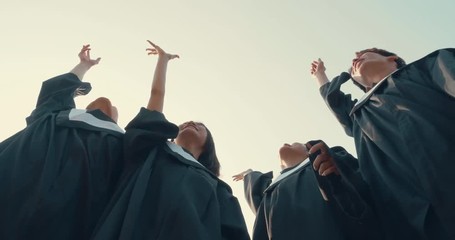 graduation students in bachelor gowns throwing mortar boards up in the air