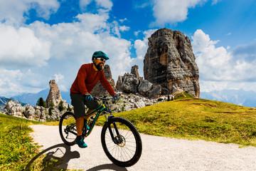 Tourist cycling in Cortina d'Ampezzo, stunning Cinque Torri and Tofana in background. Man riding MTB enduro flow trail. South Tyrol province of Italy, Dolomites.