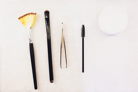 Top view of accessories for brows care and eyebrow coloring, pencil, angle brushes with natural bristles, spooly brush, tweezers and brow comb on white background. Eyebrow grooming tools.