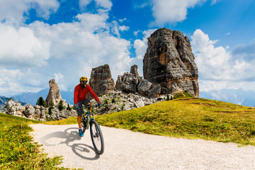 Tourist cycling in Cortina d'Ampezzo, stunning Cinque Torri and Tofana in background. Man riding MTB enduro flow trail. South Tyrol province of Italy, Dolomites.