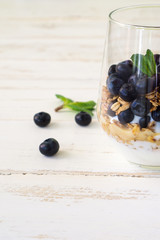 Oatmeal granola with blueberries, yogurt and mint in a glass on a white and blue rustic background with copy space