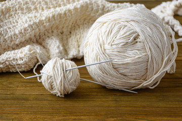 Ball of beige yarn by wool and knitting needles at home on brown wooden table