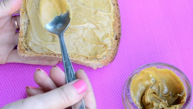 girl making a sandwich. spooning peanut butter out of a jar. Toasted bread with tasty peanut butter on purpel table