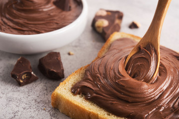Chocolate spread on slice of bread with spoon, melted cream white bowl