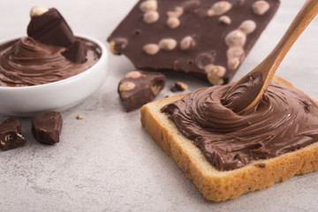 Chocolate spread on slice of bread with spoon, melted cream white bowl