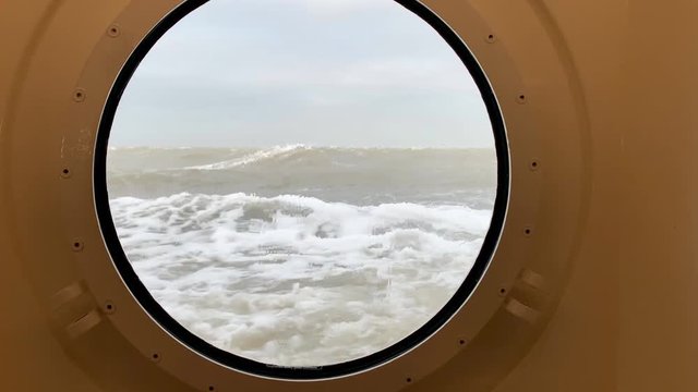 View through a porthole on a stormy sea with waves hitting the ship sailing past a red buoy at the Wadden Sea between Lauwersoog and Schiermmonnikoog