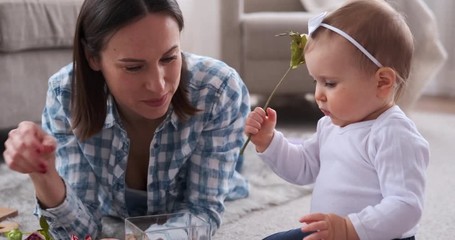 Mother and adorable baby daughter inserting rose flowers in vase