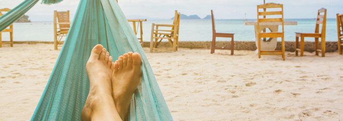 Banner with feet of a young woman in hammock on the beach. Copy Space.