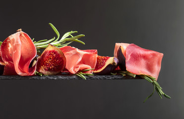 Prosciutto with figs and rosemary on a dark background.