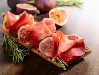 Prosciutto with figs and rosemary on a old wooden table.