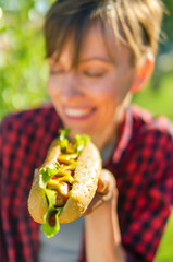 Young caucasian woman eating classic hot dog in a local park outdoors