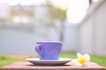 blue cup of coffee on a wooden plate with plumeria flower on a green grass with blurred background