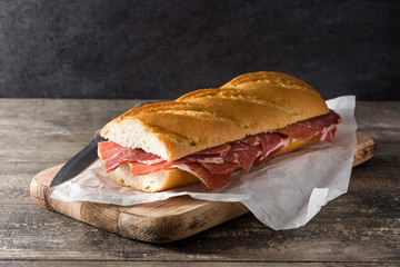 Spanish serrano ham sandwich on wooden table.