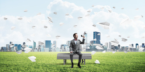 Businessman in summer park announcing something in loudspeaker and paper planes flying around