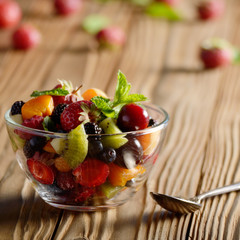 Assorted fruits in glass bowl on kitchen wooden table with spoon aside
