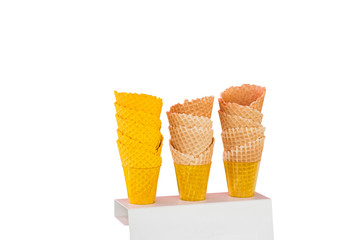 Ice cream cones made of baked wafers in the form of cones with different colors in plastic cups on a stand.