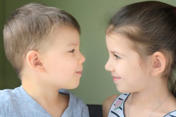 White caucasian toddler boy and girl look at each other with love on blurred neutral background. Cute little brother and beautiful sister with happiness faces looking at each other and smiling 