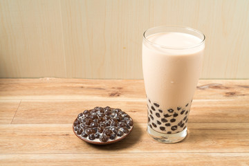 A glass cup of pearl milk tea (also called bubble tea) and a plate of tapioca ball on wooden background. Pearl milk tea is the most representative drink in Taiwan. Taiwan food . With copy space.