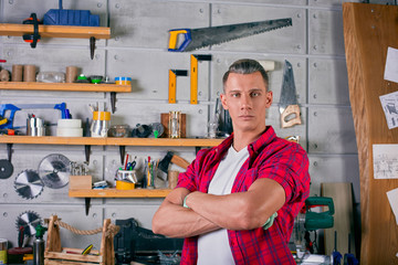 locksmith stands in the workshop on the background of the wall with shelves under the tools