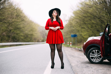 Young stylish woman wearing red dress, black hat walking on the city street in autumn. Fall fashion, elegant look. Plus size model.