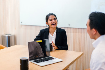An ideal Indian woman sitting near an accomplice inside a social gathering room. She is examining some system and looking immaculate in her office clothing.