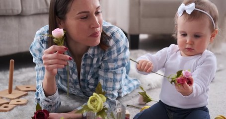 Mom and cute baby daughter inserting rose flowers in vase