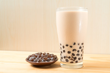 A glass cup of pearl milk tea (also called bubble tea) and a plate of tapioca ball on wooden background. Pearl milk tea is the most representative drink in Taiwan. Taiwan food . With copy space.