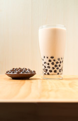 A glass cup of pearl milk tea (also called bubble tea) and a plate of tapioca ball on wooden background. Pearl milk tea is the most representative drink in Taiwan. Taiwan food . With copy space.