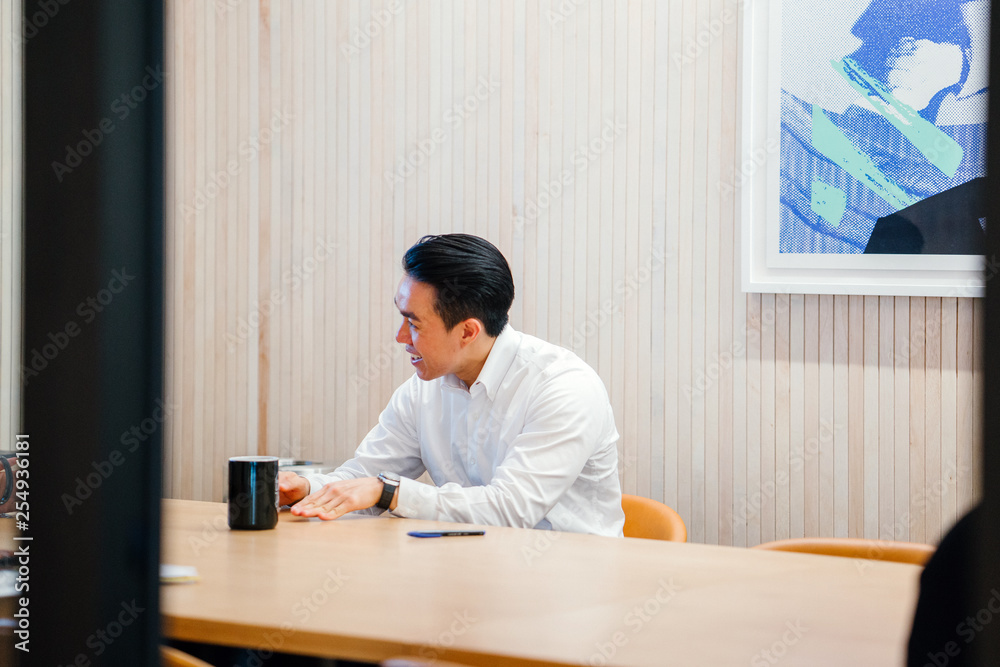 Wall mural An attractive Chinese Asian businessperson sits on the seat and stops for a moment to talk with his group amid the day. He is getting a charge out of a hot refreshment while he talks to his associates