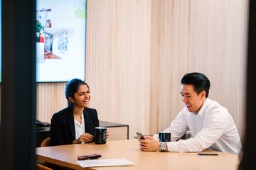 Teammate talking to each other while enjoying their coffee. They are discussing work-related stuff inside a conference room and looking good in their office attire.