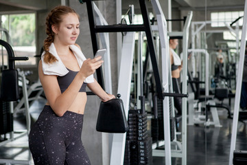 Fototapeta na wymiar young fitness woman with towel using smartphone and relaxing in gym . sport girl taking a break after exercises workout.resting