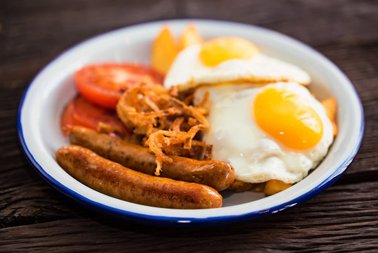 Typial breakfast with eggs, tomato, onion rings and sausage on plate