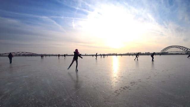 People ice skating on a frozen lake next to the river IJssel in Holland during a beautiful winter day winter. People are enjoying this typical Dutch winter activity.