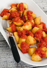 Papas Bravas, deep fried potato cubes typically served as tapas in Madrid, Spain with spicy mojo rojo, a red hot sauce made of tomatoes, bell peppers, onions and chili on white plate and wooden table