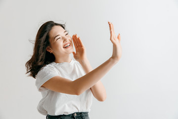 Do not miss. Young casual woman shouting. Shout. Crying emotional woman screaming ongray studio background. Female half-length portrait. Human emotions, facial expression concept.