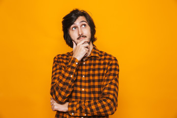 Portrait of unshaved man wearing plaid shirt touching chin and looking upward while standing...