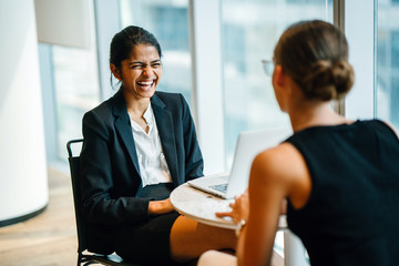 An exquisite Indian woman sitting by an accomplice inside a cafeteria. She is telling a joke with a teammate.