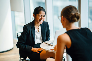 An exquisite Indian woman sitting by an accomplice inside a cafeteria. She is telling a joke with a teammate.