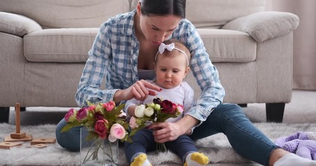 Mother and baby daughter arranging rose flowers in the living room