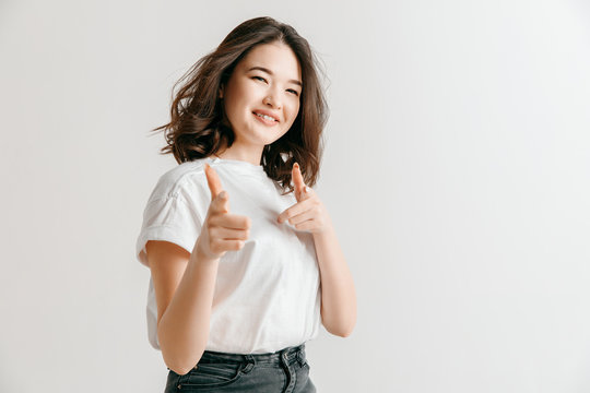 Happy asian woman standing and presenting something isolated on gray studio background. Beautiful female half-length portrait. Young emotional woman. The human emotions, facial expression concept.