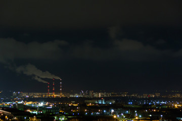 City skyline at night.Night view of a neighbourhood with low-rise apartment blocks illuminated window lights. Pipes of thermal power plant smoke