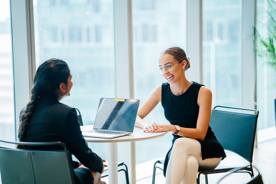 A Caucasian white woman showing her accommodating smile while on a business dialogue with an Asian woman in an office during the day. They are sharing thoughts to each other.