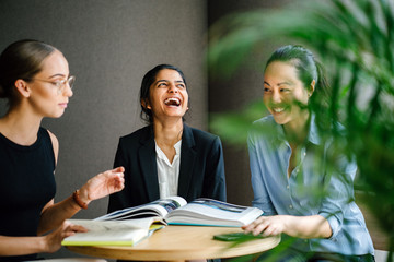 Portrait of a Caucasian woman sitting in a desk leading a casual business meeting with her team in a meeting room. They're having an animated conversation. Image taken with a blur foreground.