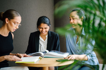 Portrait of an Asian Indian woman sitting in a desk while having a casual business meeting with her team in a meeting room. They're having an animated conversation. Image taken with a blur foreground.