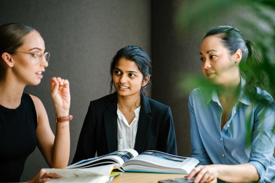 Portrait of a Caucasian woman sitting in a desk leading a casual business meeting with her team in a meeting room. The are having an animated conversation. Image taken with a blur foreground.
