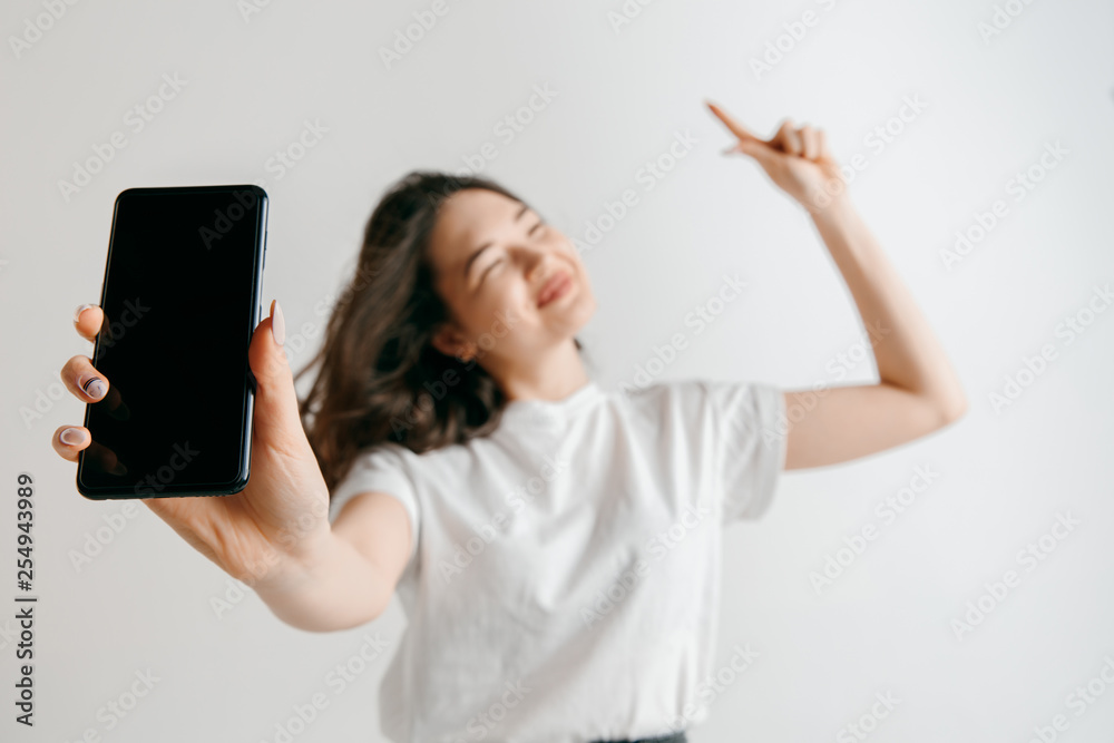 Wall mural portrait of a confident casual asian girl showing blank screen of mobile phone isolated over gray ba