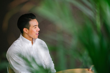Portrait of a handsome, and confident Chinese Asian businessman sitting at a table in a meeting room and having a business discussion with a person that is out of view.