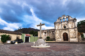 Obraz premium Church fassade ruin of Ermita de Santa Isabel and cross on plaza with dramatic cloudscape, Antigua, Guatemala