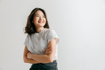 Happy asian woman standing and smiling isolated on gray studio background. Beautiful female half-length portrait. Young emotional woman. The human emotions, facial expression concept.