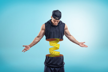 Strong muscular young man cut in half with yellow measuring tape inside on blue background